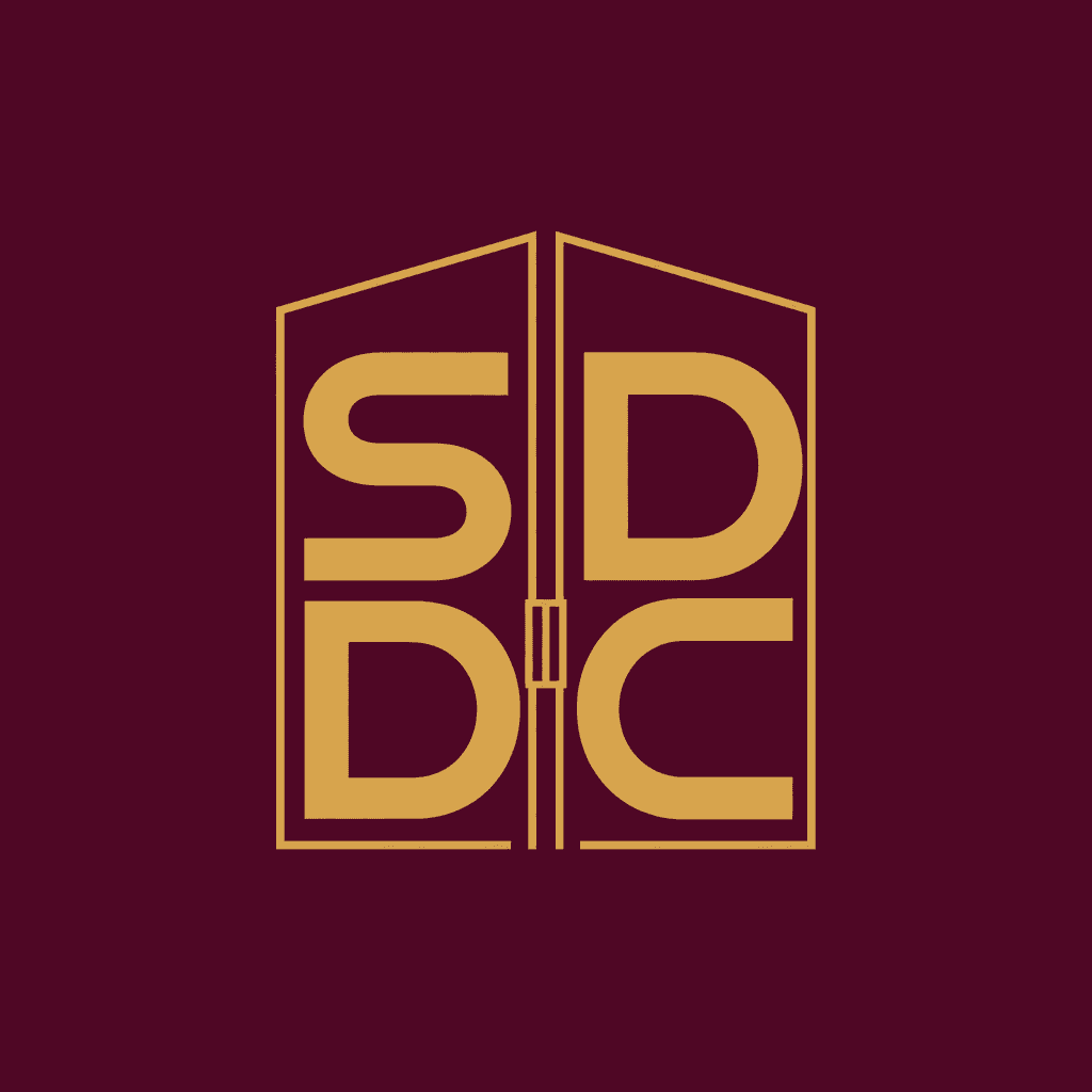 SDDC compact icon logo — gold initials with storefront geometric outline on deep burgundy background, square social profile format