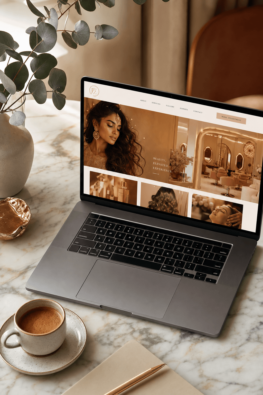 Editorial lifestyle shot of a laptop displaying an elegant salon website on a marble desk, with eucalyptus and coffee for a polished upscale aesthetic